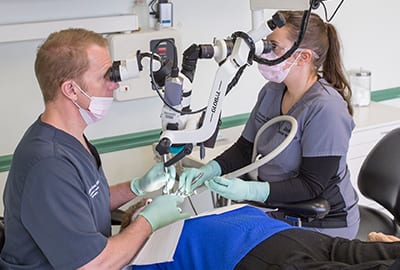 Dr Cross and staff member looking through microscope at patient on table j David cross dds