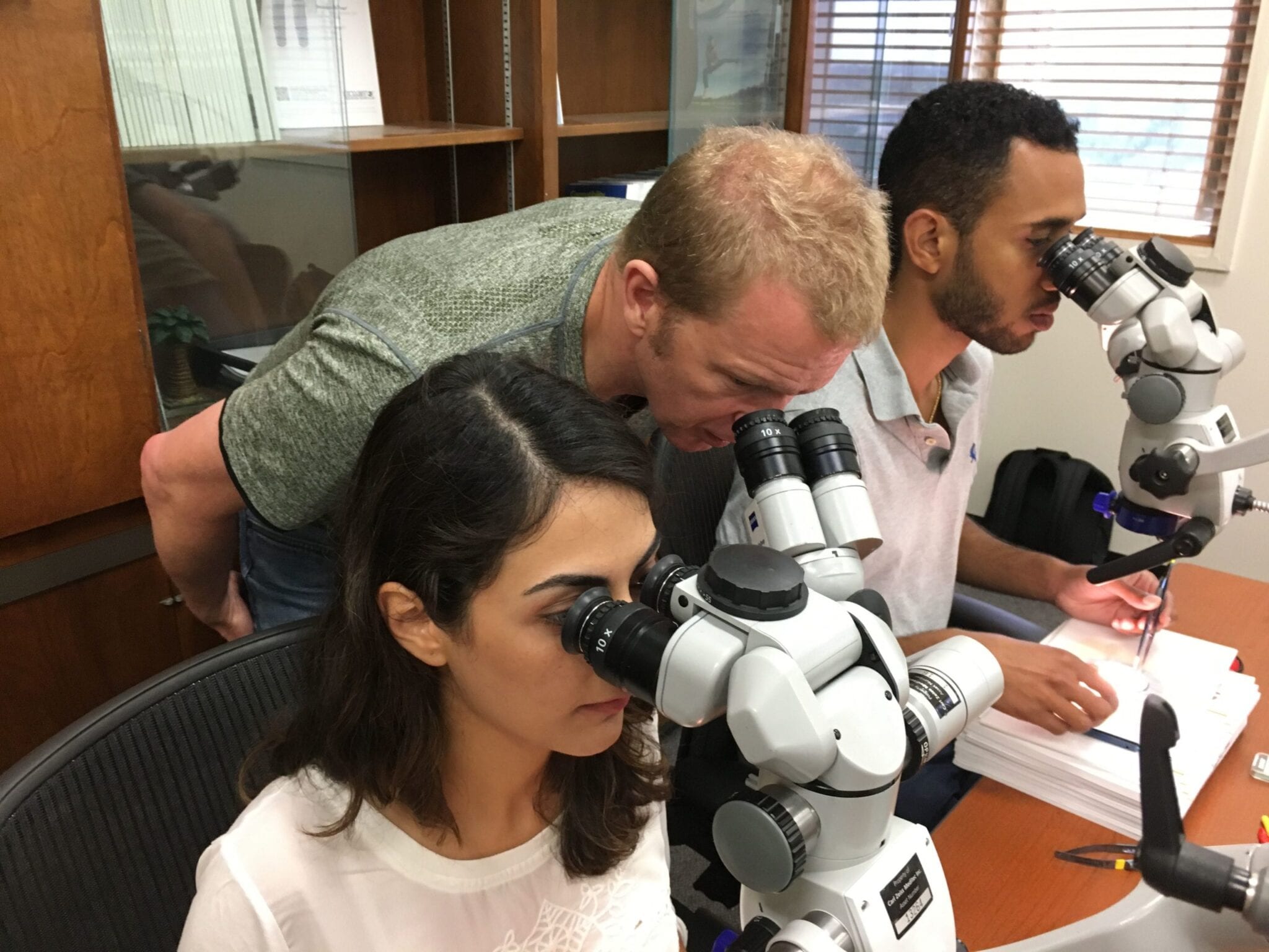 Dr. Cross Looking Through Microscope with Other Students